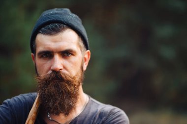 Siyah tişörtlü şık sakallı adam, kafasında kafasıyla ormanda tahta bir balta tutuyor.