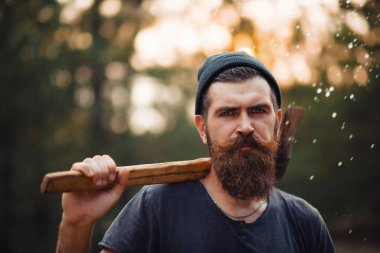 Siyah tişörtlü şık sakallı adam, kafasında kafasıyla ormanda tahta bir balta tutuyor.