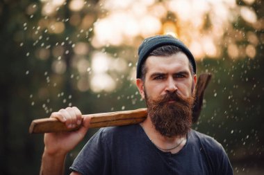 Siyah tişörtlü şık sakallı adam, kafasında kafasıyla ormanda tahta bir balta tutuyor.