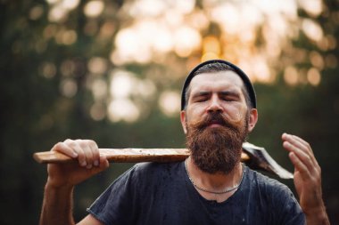 Siyah tişörtlü şık sakallı adam, kafasında kafasıyla ormanda tahta bir balta tutuyor.