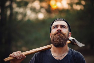 Siyah tişörtlü şık sakallı adam, kafasında kafasıyla ormanda tahta bir balta tutuyor.