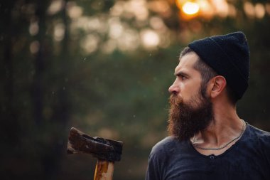 Siyah tişörtlü şık sakallı adam, kafasında kafasıyla ormanda tahta bir balta tutuyor.