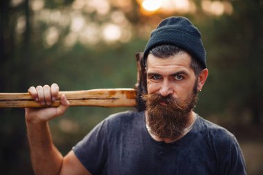 Siyah tişörtlü şık sakallı adam, kafasında kafasıyla ormanda tahta bir balta tutuyor.