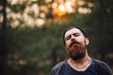 Siyah tişörtlü şık sakallı adam, kafasında kafasıyla ormanda tahta bir balta tutuyor.