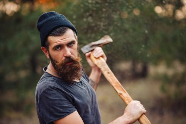 Siyah tişörtlü şık sakallı adam, kafasında kafasıyla ormanda tahta bir balta tutuyor.