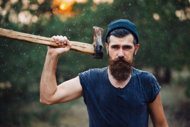 Siyah tişörtlü şık sakallı adam, kafasında kafasıyla ormanda tahta bir balta tutuyor.