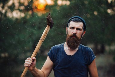 Siyah tişörtlü şık sakallı adam, kafasında kafasıyla ormanda tahta bir balta tutuyor.