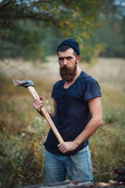 Siyah tişörtlü şık sakallı adam, kafasında kafasıyla ormanda tahta bir balta tutuyor.