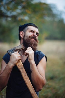Siyah tişörtlü şık sakallı adam, kafasında kafasıyla ormanda tahta bir balta tutuyor.