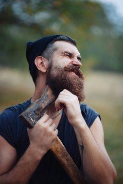 Siyah tişörtlü şık sakallı adam, kafasında kafasıyla ormanda tahta bir balta tutuyor.