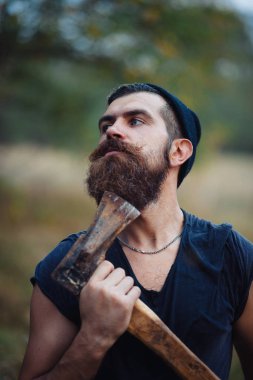 Siyah tişörtlü şık sakallı adam, kafasında kafasıyla ormanda tahta bir balta tutuyor.