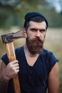 Siyah tişörtlü şık sakallı adam, kafasında kafasıyla ormanda tahta bir balta tutuyor.