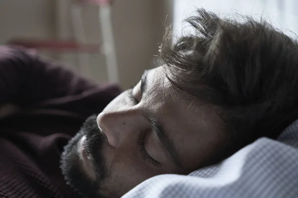 Handsome man sleeping in his bedroom. Man sleeping with alarm clock in foreground. Serene latin man sleeping peacefully.