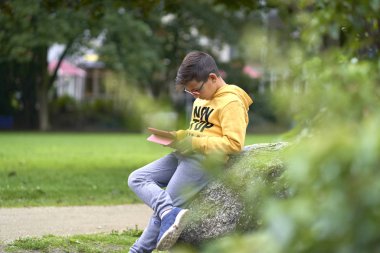 Sarı kazaklı çocuk sokakta tabletiyle sörf yapıyor.