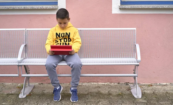 Niño con sudadera amarilla surfeando con su tablet en la calle —  Fotos de Stock