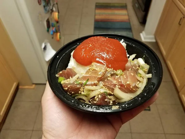 Mão segurando tigela de atum cru e cebolas e molho vermelho na cozinha — Fotografia de Stock