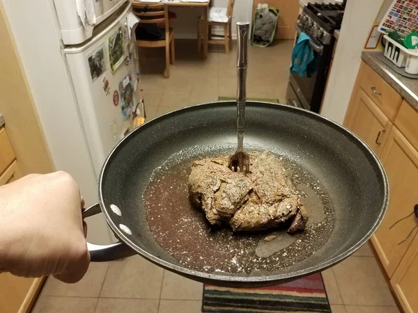 Poêle à frire à main avec boeuf et jus et fourchette dans la cuisine — Photo