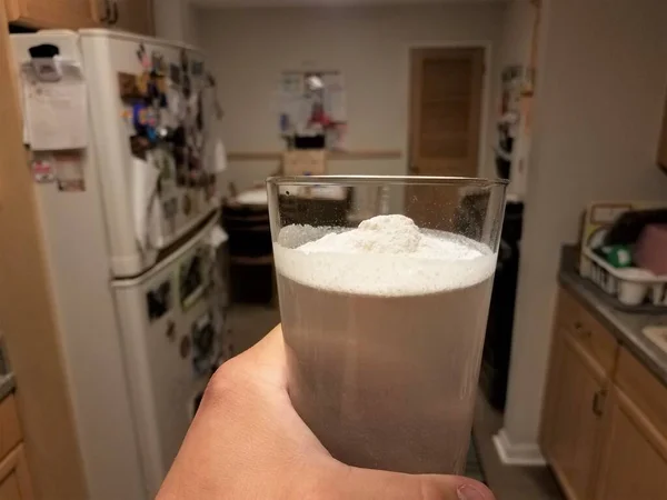 Mão segurando vidro de água e pó branco na cozinha — Fotografia de Stock