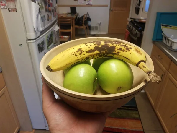 Mão segurando tigela de maçãs e banana na cozinha — Fotografia de Stock