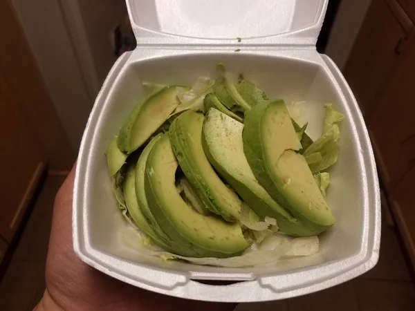 Hand houden van groene avocado plakjes met sla in schuim container — Stockfoto