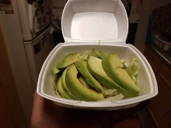 Mão segurando fatias de abacate verde com alface em recipiente de espuma — Fotografia de Stock