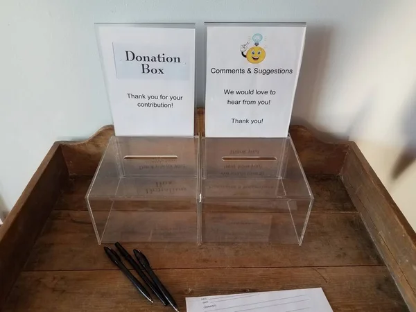 plastic donation and comment box with pen and paper on desk