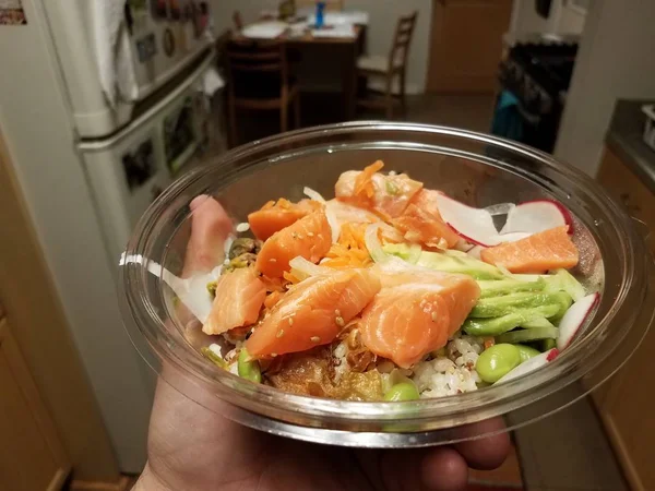 Hand holding bowl of salmon sushi and rice and avocado in kitchen — Stock Photo, Image