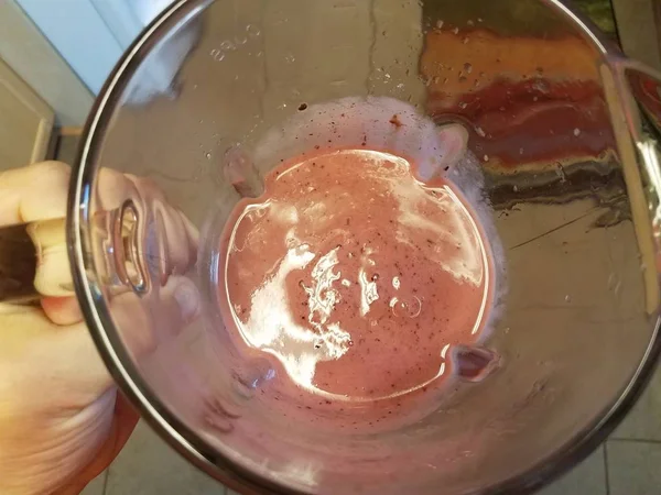 Mão segurando liquidificador de vidro com líquido de smoothie rosa na cozinha — Fotografia de Stock