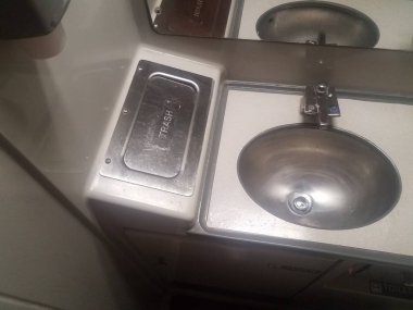 Trendeki banyoda metal lavabo ve çöp tenekesi