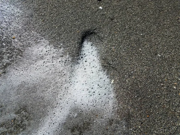 Pegada na pista em areia cinzenta molhada na praia com bolhas — Fotografia de Stock