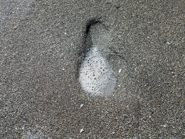 Voetafdruk op spoor in nat grijs zand op het strand met bubbels — Stockfoto