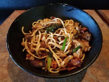 asian noodles in bowl with beef, pork, bacon, and vegetables on table