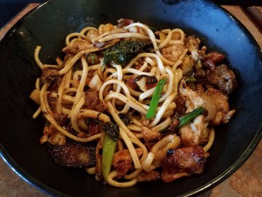 asian noodles in bowl with beef, pork, bacon, and vegetables on table
