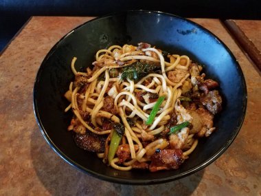 asian noodles in bowl with beef, pork, bacon, and vegetables on table