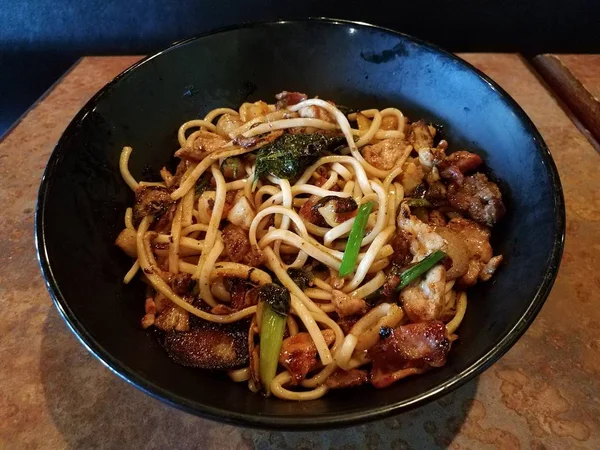 Asian noodles in bowl with beef, pork, bacon, and vegetables on table — Photo