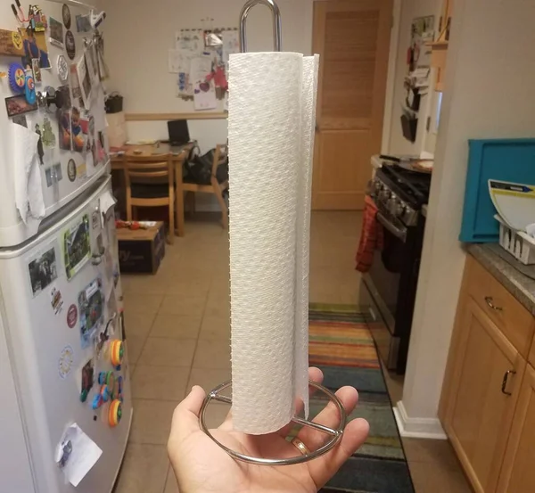 Mano sosteniendo toallas de papel en la cocina cerca del refrigerador —  Fotos de Stock