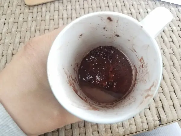 Hand holding white cup with melted chocolate and brown table — Foto de Stock