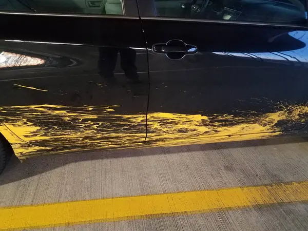 Black car with yellow paint splatter and cement with line — Foto de Stock