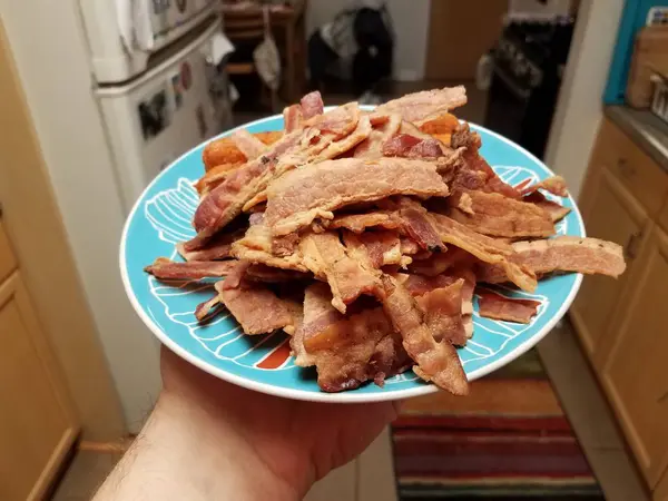 Mão segurando pilha de carne de bacon e rolo de frango na placa azul — Fotografia de Stock