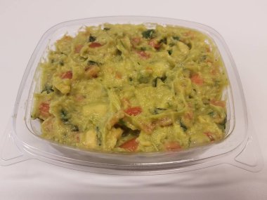 Beyaz yüzeyde avokado veya guacamole içeren plastik bir kap.
