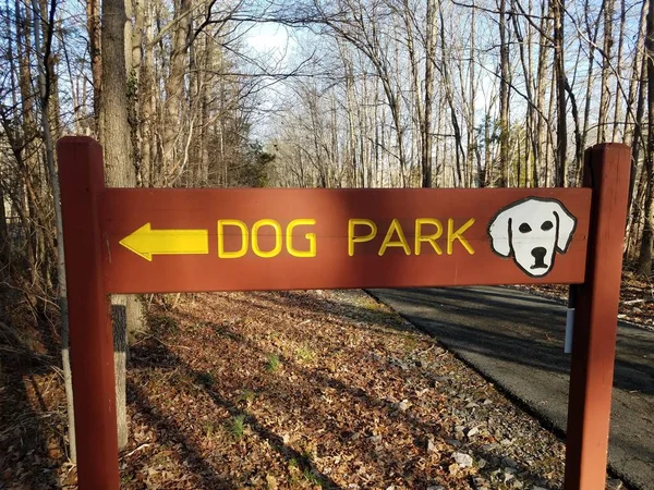 Letrero de parque de perros de madera con flecha amarilla y sendero de asfalto y árboles —  Fotos de Stock