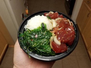 hand holding bowl of raw tuna and green seaweed and rice in kitchen