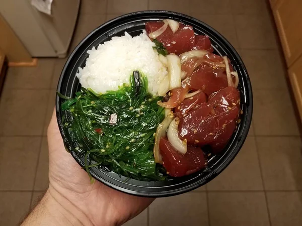 Hand holding bowl of raw tuna and green seaweed and rice in kitchen — 스톡 사진