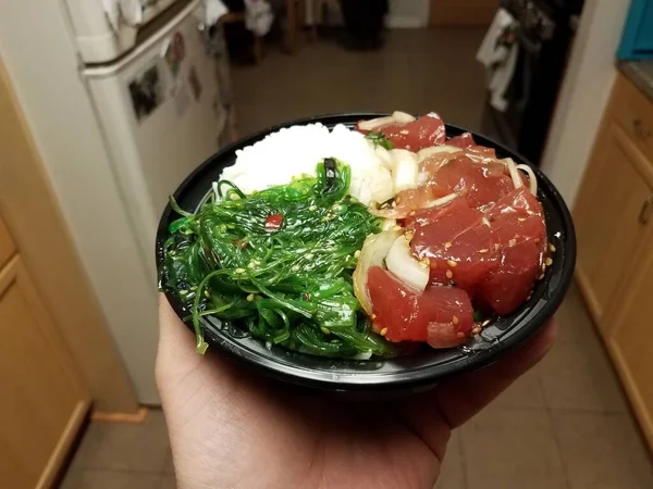 Hand holding bowl of raw tuna and green seaweed and rice in kitchen — 스톡 사진