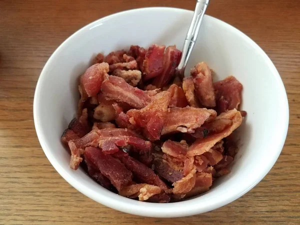 Bowl of bacon meat with utensil on wood table — Stock Photo, Image