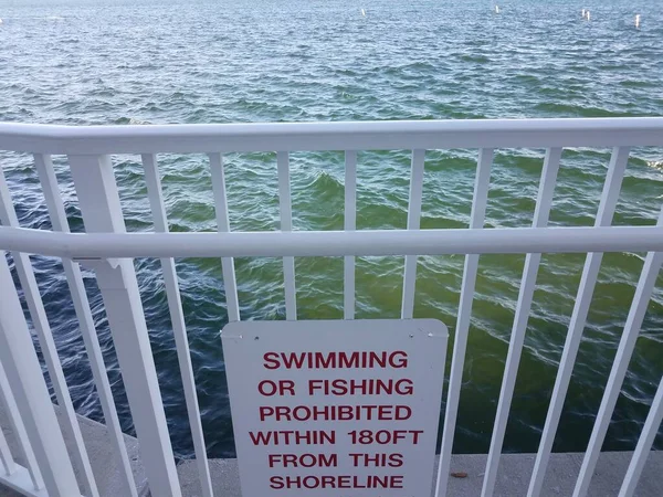 Swimming or fishing prohibited sign on railing with water — Stock fotografie
