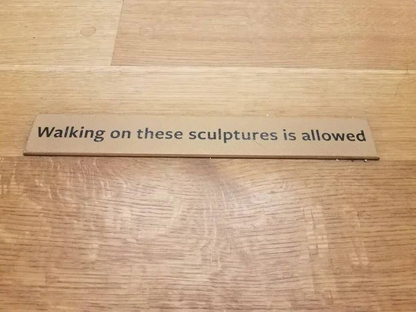 Walking on these sculptures is allowed sign on wood floor — Zdjęcie stockowe