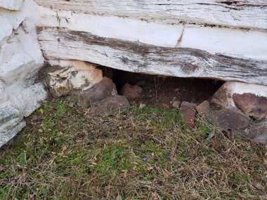 crawl space or hole underneath white wood and stone house