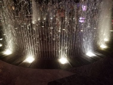 people playing in water fountain jets with lights at night