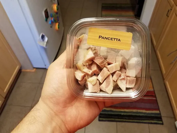 Hand holding container of pancetta meat in kitchen — 图库照片